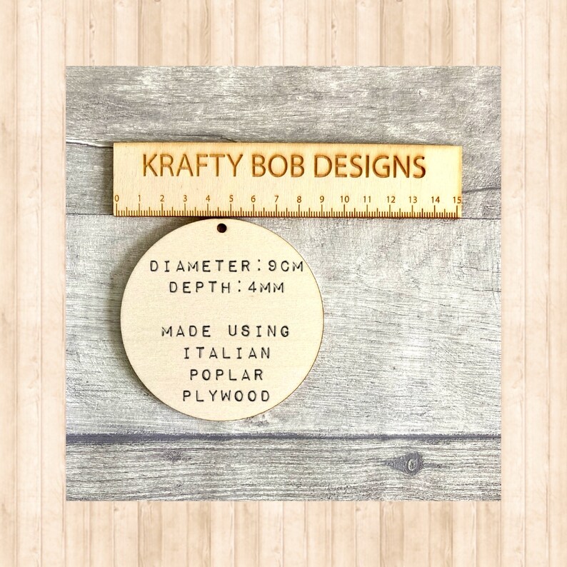 May include: A circular light-colored wooden disc with a small hole at the top. The text on the disc reads: DIAMETER: 9CM, DEPTH: 4MM, MADE USING ITALIAN POPLAR PLYWOOD. A wooden ruler labeled KRAFTY BOB DESIGNS is positioned above the disc for scale.