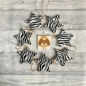 May include: A decorative garland featuring star-shaped ornaments with a black and white zebra print. A small wooden square with a dog portrait and the text "KRAFTY BOB" is in the centre. The stars are strung together with twine.