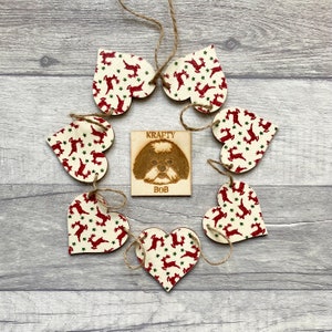 May include: A set of six wooden heart-shaped ornaments featuring a red reindeer and green star pattern, connected by twine. In the center is a square wooden plaque with a wood-burned illustration of a dog and the text KRAFTY BOB.