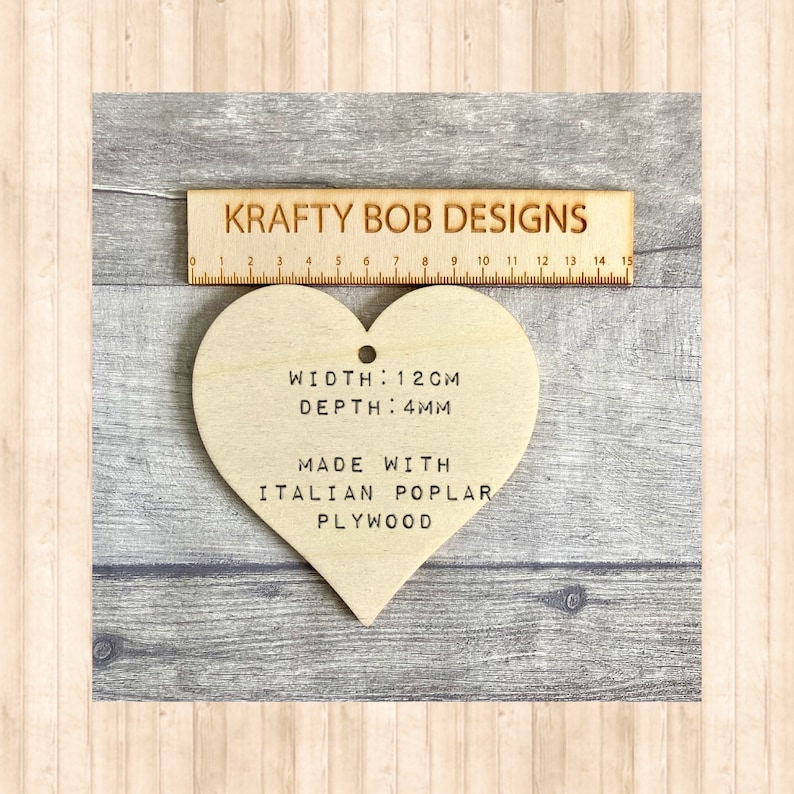 A wooden heart-shaped decoration with the text 'WIDTH: 12CM', 'DEPTH: 4MM', 'MADE WITH', 'ITALIAN POPLAR PLYWOOD'.