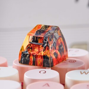 K&ouml;nnte beinhalten: Eine Harz-Tastenkappe mit einem farbenfrohen Bild eines japanischen Tempels und einer Berglandschaft. Die Tastenkappe liegt auf einer Tastatur mit rosa und wei&szlig;en Tasten.