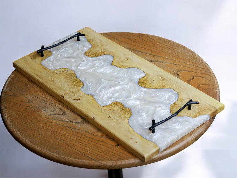 May include: A rectangular wooden serving tray with a white resin inlay and black metal handles. The resin has a swirling pattern.