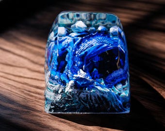 Può includere: Un keycap in resina blu con un design dettagliato di un drago in un motivo nuvoloso vorticoso. Il keycap è trasparente e mostra il drago in dettaglio.