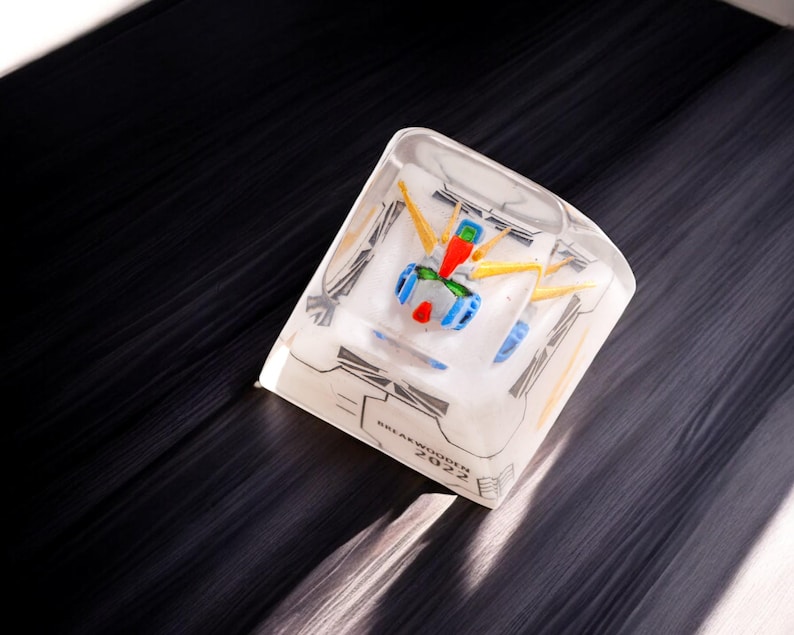 May include: A clear resin cube keycap with a white and yellow robot figure inside. The keycap has the text "BREAKWATER 2022" printed on the bottom.