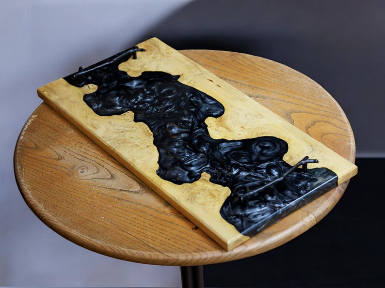 May include: A wooden serving tray with a black epoxy resin inlay. The tray has two metal handles.
