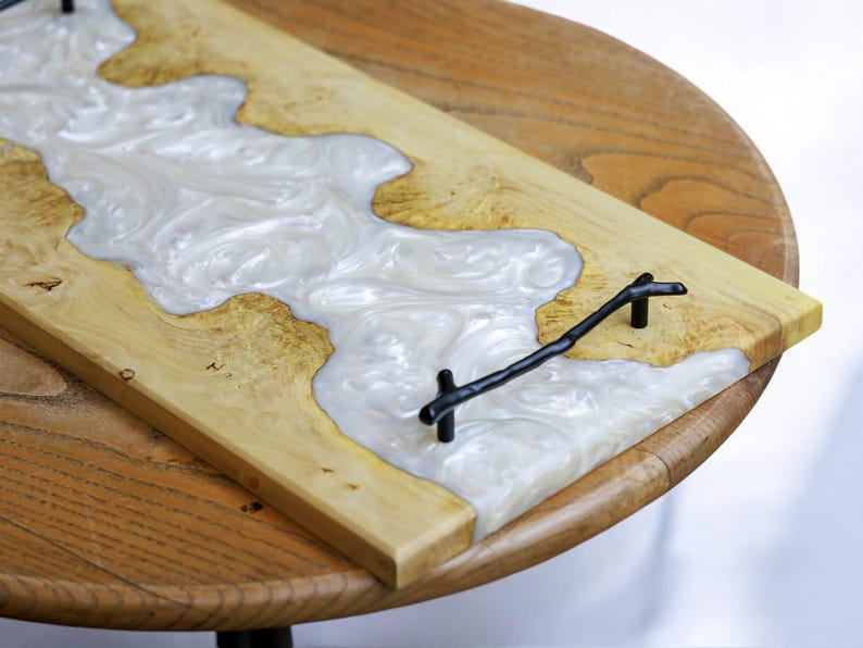May include: A wooden serving tray with a white resin inlay and black metal handles. The resin has a swirling pattern.