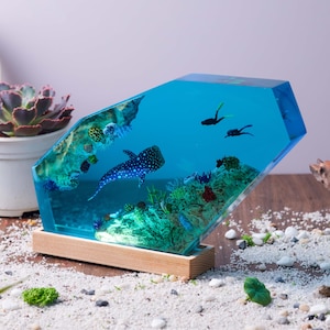 May include: A blue resin sculpture of an ocean scene with a whale shark, coral, and small fish. The sculpture is on a wooden base.