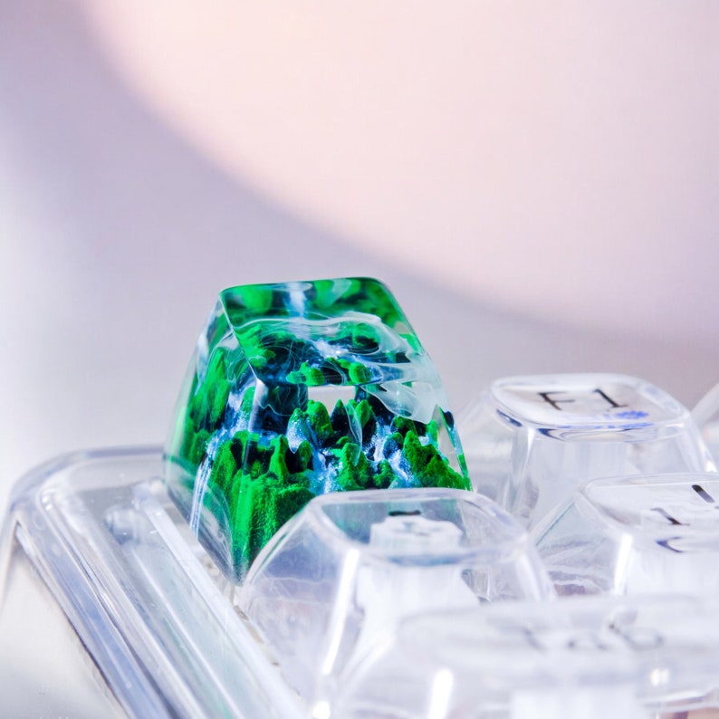 May include: A green and blue resin keycap with a swirling pattern, sitting on a clear plastic keyboard.