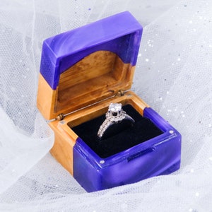 May include: A purple and wood ring box with a diamond engagement ring inside.