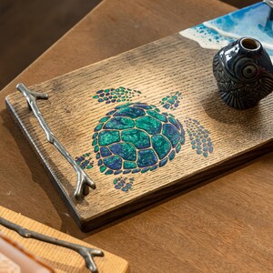 May include: A wooden serving tray with a green and blue sea turtle design. The tray has a branch-shaped handle.