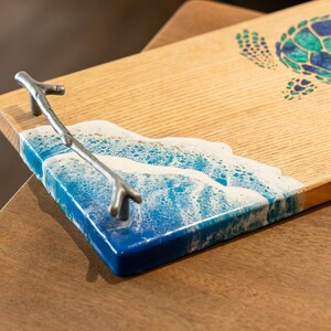 May include: A wooden serving tray with a blue and white resin wave design and a silver metal branch handle. The tray has a sea turtle design on the top.