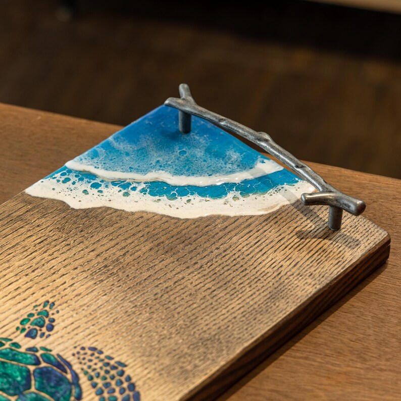 May include: A wooden serving tray with a blue and white resin ocean wave design and a metal branch handle. The tray features a green and blue turtle design.