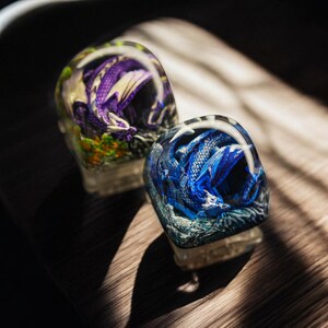 May include: Two clear glass paperweights with detailed dragon figurines inside. One dragon is purple and the other is blue.