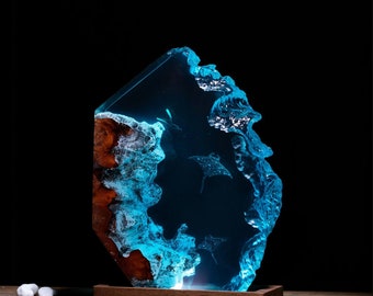 Könnte beinhalten: Eine blaue Harzskulptur mit einem Holzsockel. Das Harz zeigt ein Wellendesign mit Silhouetten von Mantarochen. Der Sockel ist mit "Breakwooden" beschriftet.