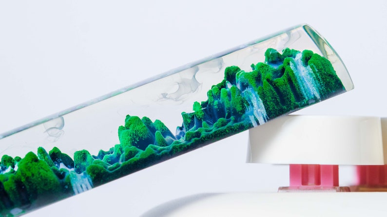 May include: A clear glass tube filled with a green and blue liquid that resembles a landscape. The liquid is moving and swirling inside the tube.