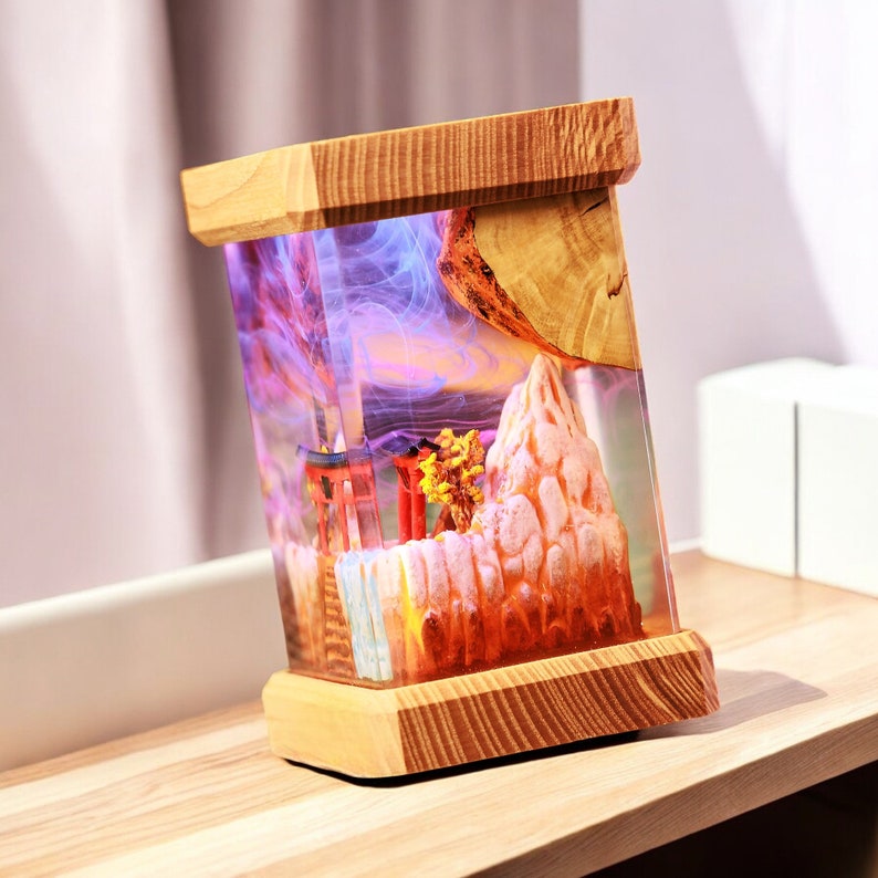 Op de afbeelding: Een houten lampenvoet met een transparante harsinzet met een miniatuur-berglandschap met een rode torii-poort en paarse en roze rook.