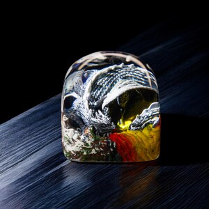 May include: A clear glass paperweight with a detailed dragon sculpture inside. The dragon is black, white, and yellow with red accents.