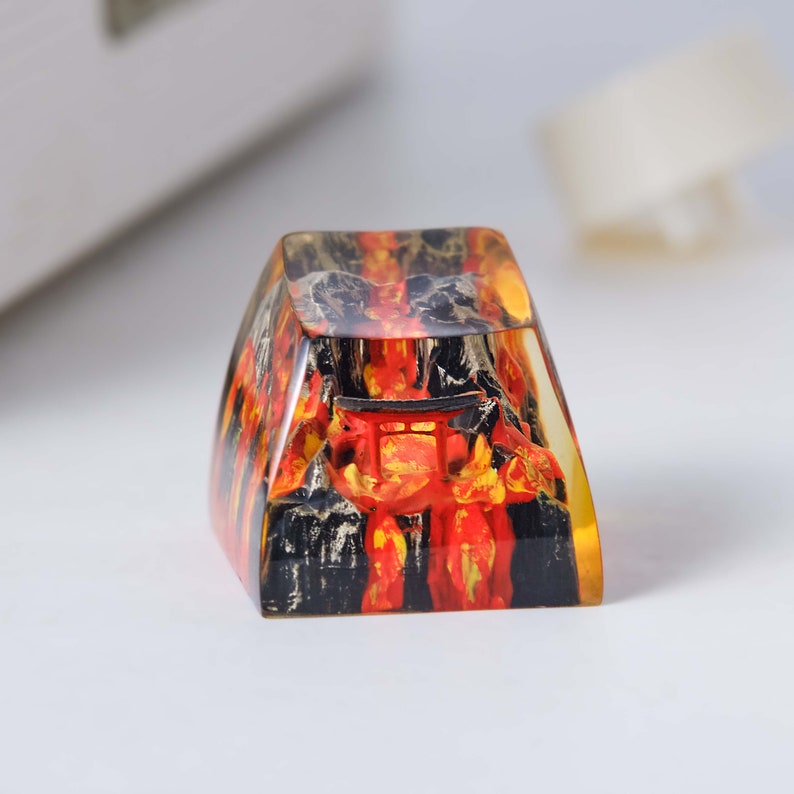 K&ouml;nnte beinhalten: Ein transparenter Harz-Tastenkappen mit einem roten und schwarzen Bild eines japanischen Tempeltors. Die Tastenkappe ist in Form einer traditionellen Tastaturtaste geformt.