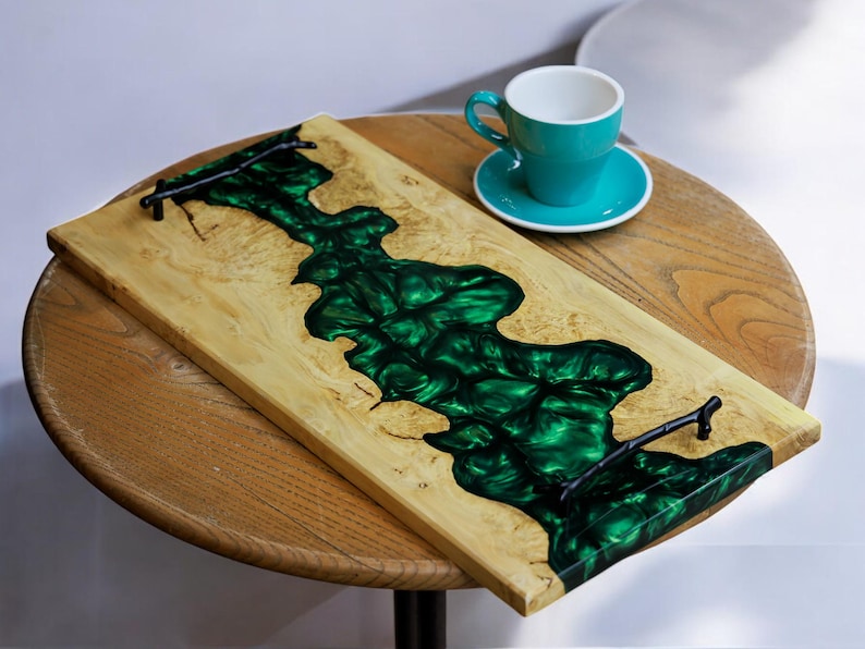 May include: A wooden serving tray with a green epoxy resin inlay and black metal handles. The tray is on a wooden table.