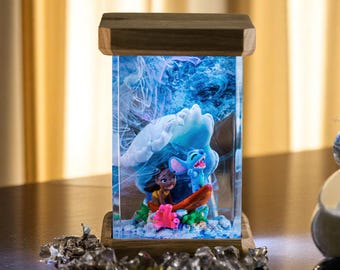 Puede incluir: Una pieza de arte de resina rectangular e iluminada con personajes de la película animada Lilo & Stitch. La obra de arte incluye una base y una parte superior de madera, con un diseño de medusa azul y blanco en el fondo. Los personajes están en un bote.