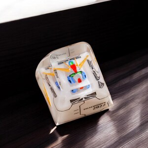 May include: A clear plastic cube with a white and blue robot figurine inside. The cube has black text that reads "BREAKTHROUGH IN 2022".