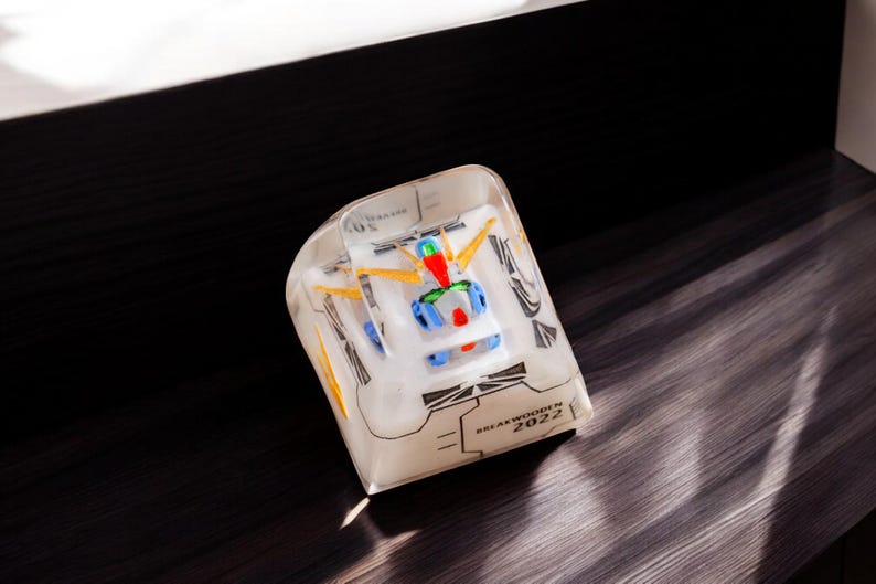 May include: A clear plastic cube with a white and blue robot figurine inside. The cube has black text that reads "BREAKTHROUGH IN 2022".