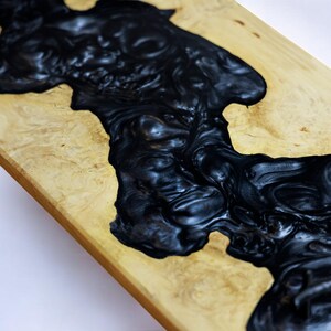 May include: A wooden table top with a black epoxy resin river flowing through it. The resin has a swirling, marbled effect.