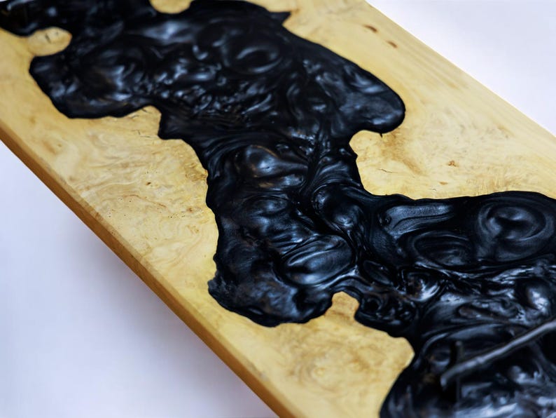 May include: A wooden table top with a black epoxy resin river flowing through it. The resin has a swirling, marbled effect.