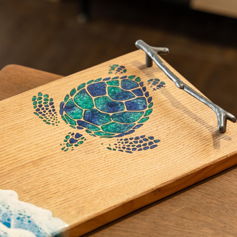 May include: A wooden serving tray with a blue and green sea turtle design and a silver twig handle.