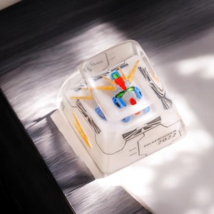 May include: A clear plastic keycap with a white and blue robot design. The keycap has the text "BREAK WOKEN 2022" printed on it.
