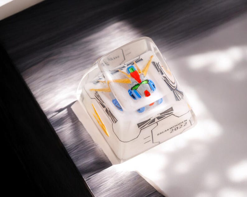 May include: A clear plastic keycap with a white and blue robot design. The keycap has the text "BREAK WOKEN 2022" printed on it.