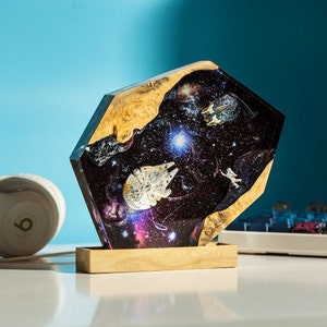 Könnte beinhalten: Ein Harz-Kunstwerk mit einer Galaxie-Szene mit Sternen, Planeten und Raumschiffen. Das Harz ist klar und hat eine glänzende Oberfläche. Das Stück ist auf einem Holzsockel montiert.