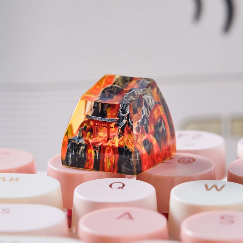 K&ouml;nnte beinhalten: Eine Harz-Tastenkappe mit einem farbenfrohen Bild eines japanischen Tempels und einer Berglandschaft. Die Tastenkappe liegt auf einer Tastatur mit rosa und wei&szlig;en Tasten.