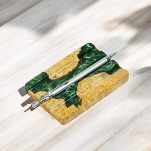 May include: A green and brown resin pen holder with a silver pen resting inside. The holder has a wavy, organic design.