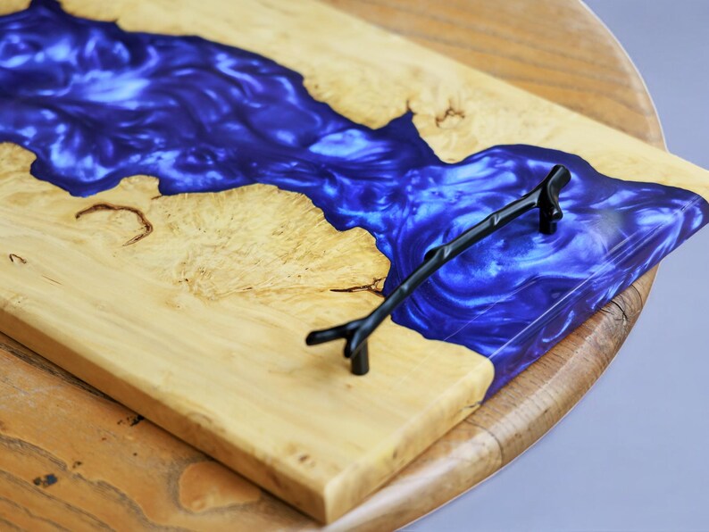 May include: A wooden serving tray with a blue resin inlay and a black metal handle. The resin has a swirling pattern.