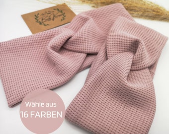 May include: A pink knotted headband made of a waffle-knit fabric. The headband is shown folded in half. The text "Wähle aus 16 FARBEN" is visible on the headband.
