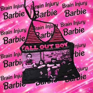 Pode incluir: Top preto com detalhes em listras rosa e preto e um gráfico da banda Fall Out Boy. O top apresenta o texto "FALL OUT BOY" e "KE THIS TO YOUR GRAVE". O fundo é rosa com as palavras "Brain Injury Barbie".