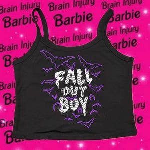 May include: Black tank top with the text "FALL OUT BOY" in white, surrounded by purple bat silhouettes. The top has thin straps and a scoop neckline. The background is pink with the words "Brain Injury" and "Barbie".