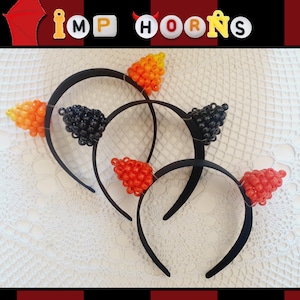 May include: Black headbands with beaded devil horns in orange, red, and black. The horns are made of small, round beads. The word "IMP HORNS" is spelled out in colorful letter beads above the headbands.