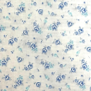 May include: A white fabric featuring a repeating pattern of small, delicate blue and light blue roses. The floral design is scattered across the surface, creating a soft, consistent texture with a woven appearance throughout the material.