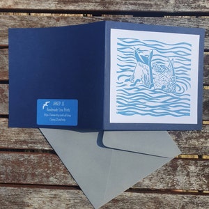 May include: A blue and white linocut print of two sea creatures swimming in the ocean. The print is on a white card with a blue border. The card is folded in half and has a blue envelope.