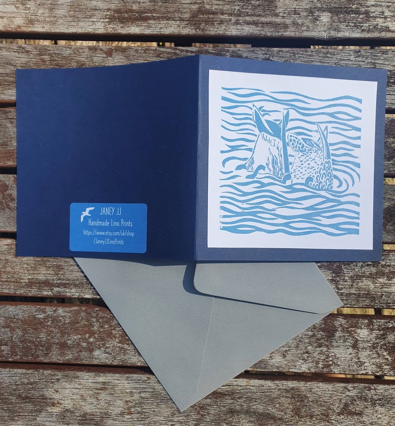 May include: A blue and white linocut print of two sea creatures swimming in the ocean. The print is on a white card with a blue border. The card is folded in half and has a blue envelope.