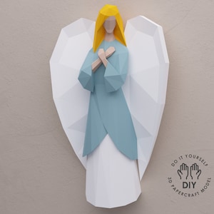 May include: A papercraft model of an angel with white wings, a blue dress, and yellow hair. The model is labeled "Do It Yourself 3D Papercraft Model DIY".