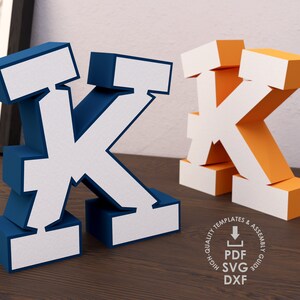May include: Two 3D papercraft letters, both the letter K. One is blue with white accents, the other is orange with white accents. Both letters are made of paper and are designed to be assembled. The image also includes a circle with the text "High Quality Templates & Assembly Guide PDF SVG DXF".