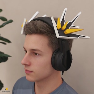 May include: Black over-ear headphones featuring decorative, angular attachments on the headband. The attachments are white with black accents and prominent yellow, geometric, spike-like elements extending upward from the top of the headset.
