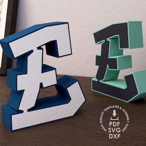 May include: Two 3D printable models of the British pound symbol. The model on the left is blue with white lettering. The model on the right is green with black lettering. Both models are on a wooden surface. High quality templates & assembly guide. PDF, SVG, DXF.
