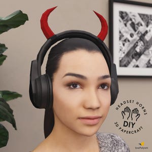 Può includere: Una persona indossa cuffie nere con corna rosse da diavolo. L'immagine include il testo "HEADSET HORNS DIY PAPERCRAFT". Lo sfondo include una stampa in bianco e nero incorniciata e una pianta verde.