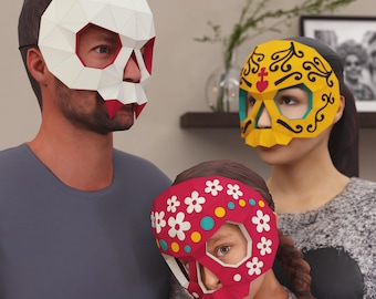 Puede incluir: Tres máscaras de calavera de papel en blanco, amarillo y rojo. La máscara blanca tiene detalles rojos, la máscara amarilla tiene detalles turquesa y negro, y la máscara roja está decorada con flores blancas y puntos de colores. Las máscaras son usadas por tres personas.
