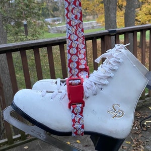 May include: White ice skates with a red and white Santa Claus pattern strap. The strap has a red plastic buckle. The skates have a black base and silver blades.