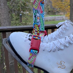 May include: White ice skates with a red and blue comic book print strap attached to the top of the skate. The strap has the words "POW!" and "BIFF!" printed on it.